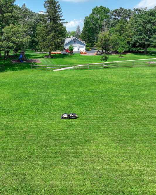 Black and yellow robotic lawn mower by Yarbo on lush green grass in a spacious backyard, side view.