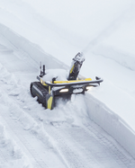 Black and yellow robotic snow blower by Yarbo clearing deep snow, tracked base with illuminated headlights, side view in action