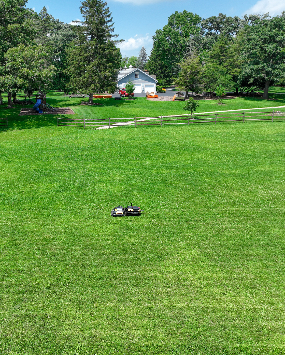 Black and yellow robotic lawn mower by Yarbo on lush green grass in a spacious backyard, side view.