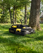 Black and yellow RTK antenna-equipped robotic lawn mower by YARBO, featuring tank treads, dual antennas, and side view on grass near tree.